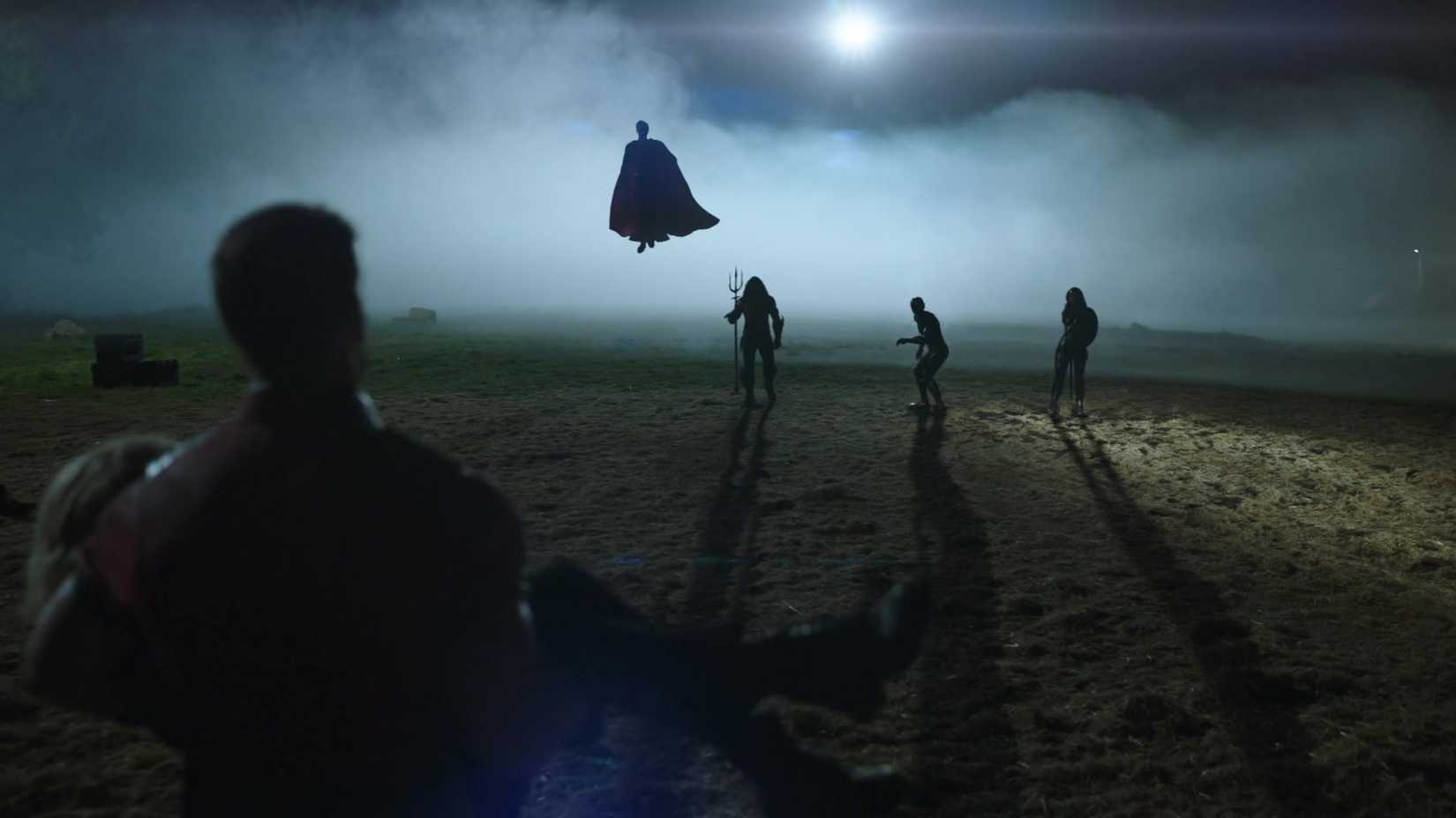 शांतिदूत (जॉन सीना), पीछे से देखा गया क्योंकि वह एक बेहोश टीम के साथी को एक लड़ाई से दूर ले जाता है, सुपरमैन, एक्वामैन, फ्लैश और वंडर वुमन के सिल्हूट वाले आंकड़ों से संपर्क करता है।