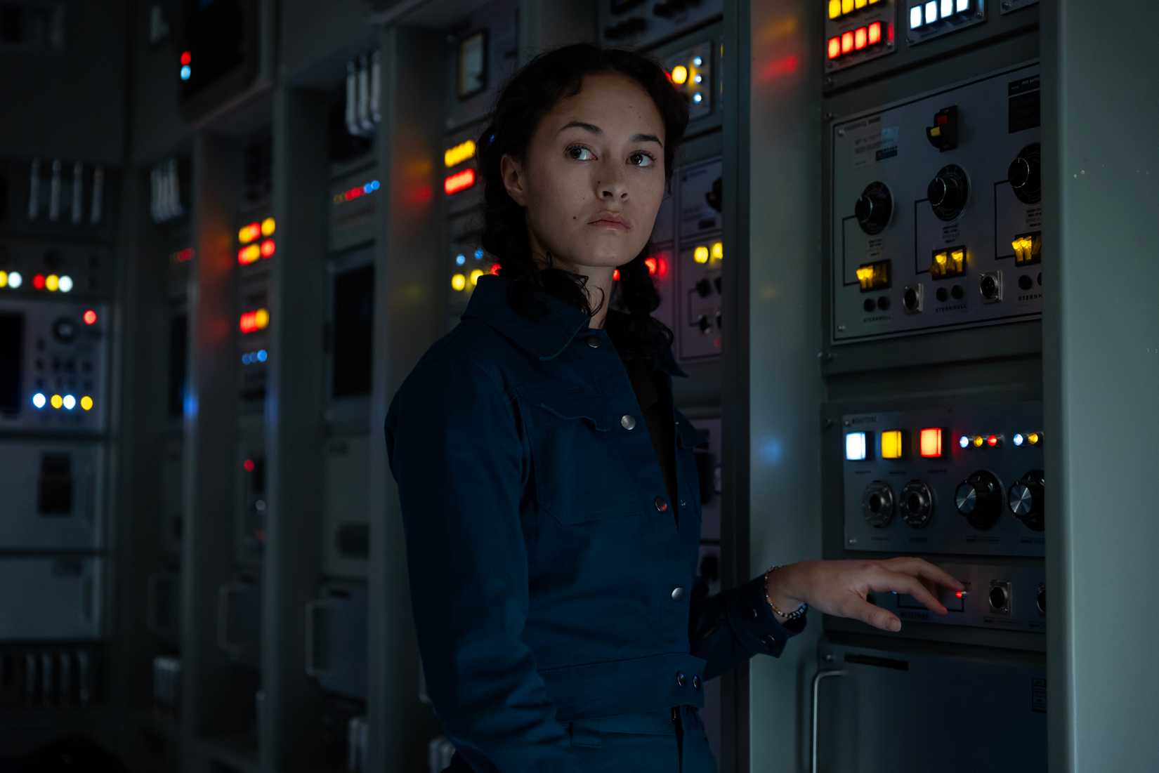 Curly (Erana James), a woman in a dark jumpsuit, stands pensively in front of a bank of computers in episode 4 of Alien: Earth