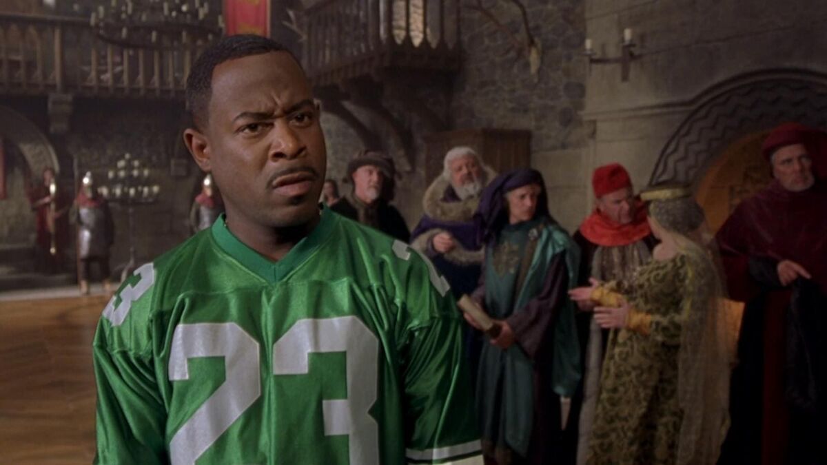 A screenshot of a man in a football jersey among people dressed in medieval wardrobe. Martin Lawrence in Black Knight 2001