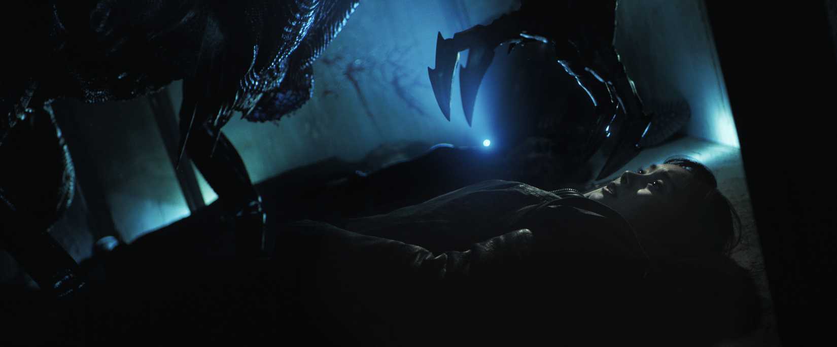 An alien creature leans over a terrified woman with an outstretched claw