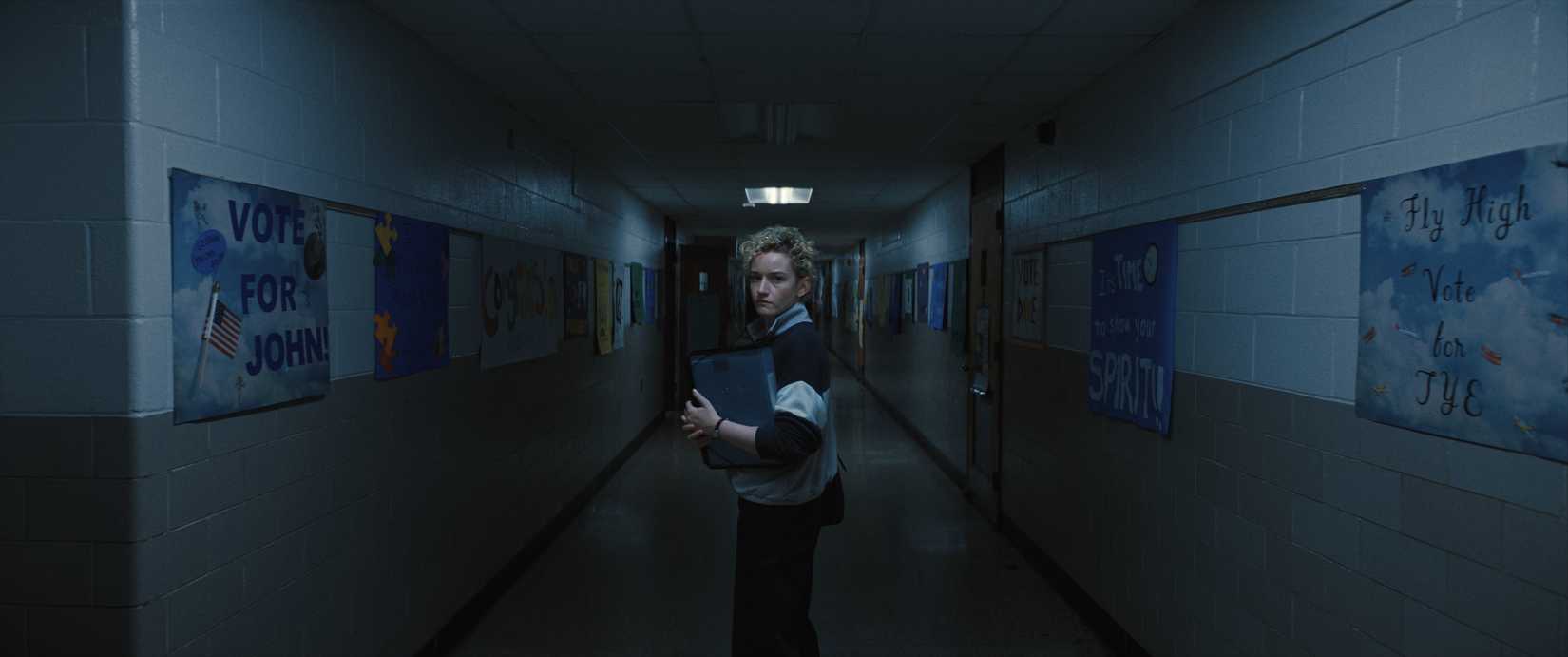 A pale woman, Justine (Julia Garner) walks down a dark hallway in an elementary school in Weapons