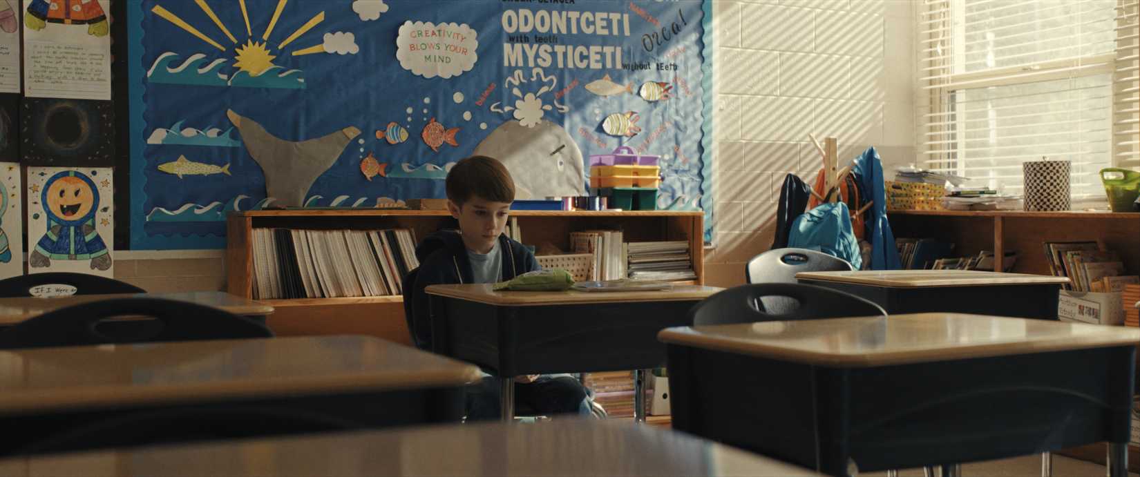 A third-grader, Alex, sits at his desk in an otherwise empty classroom in Weapons