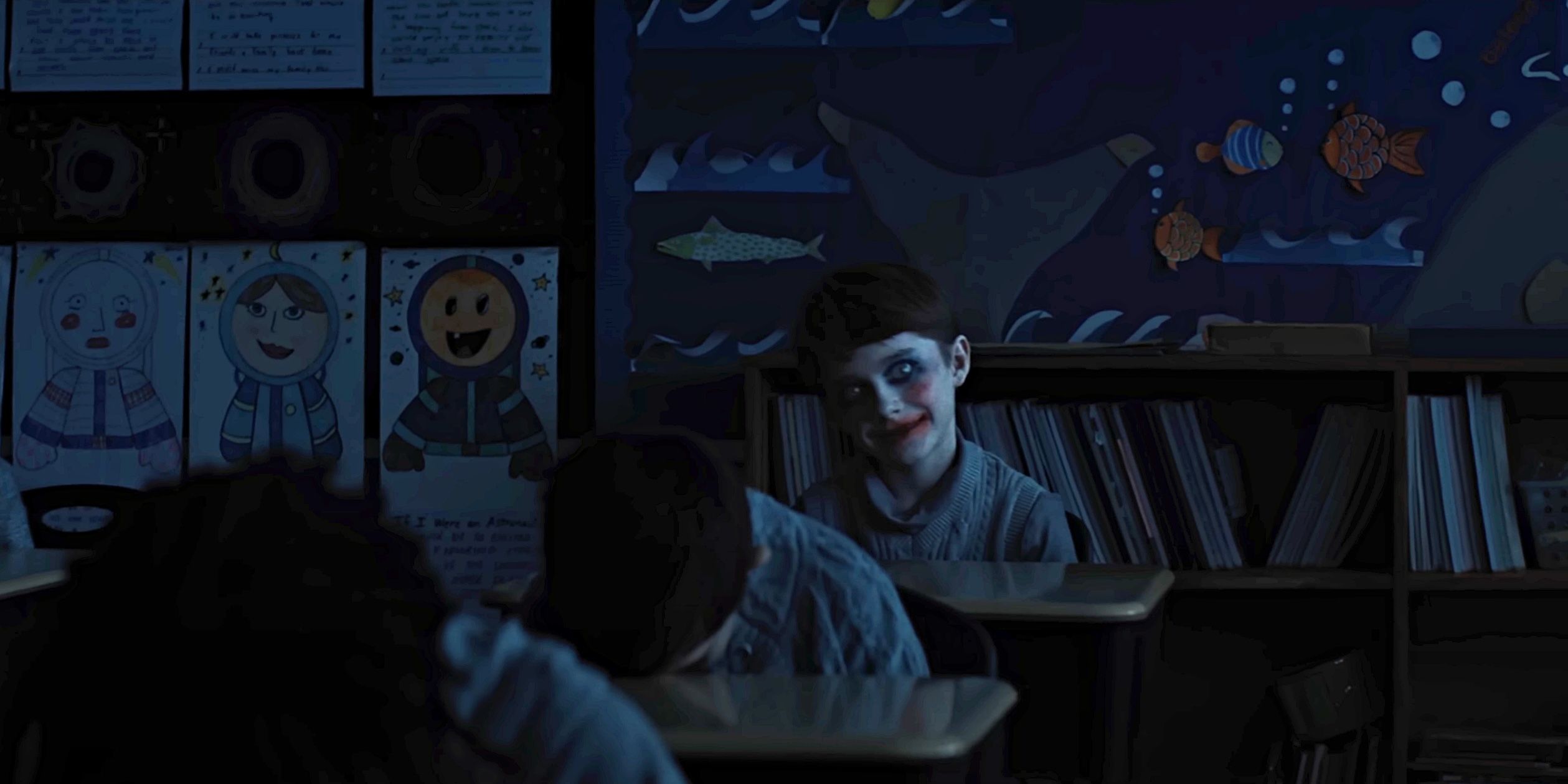 A creepy kid smiles with makeup on in a classroom in Weapons