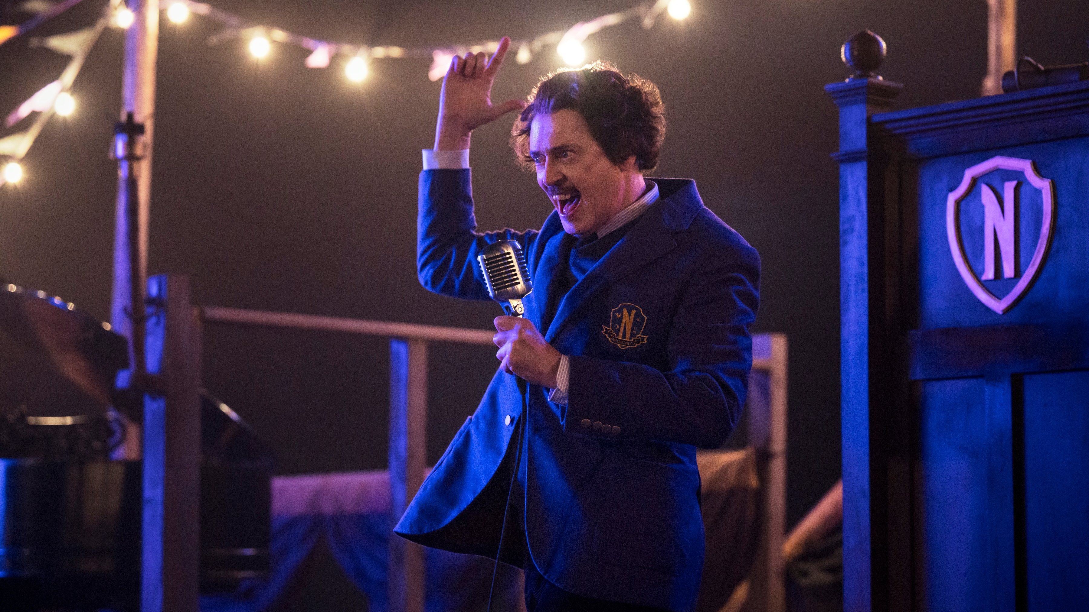 Steve Buscemi as Barry Dort stands on stage holding a microphone in Wednesday