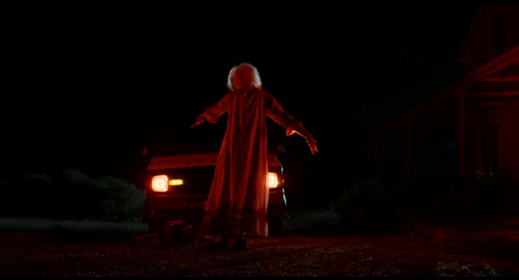 In a scene from the horror movie X, Pearl, an elderly woman played by Mia Goth, dances in front of a car's headlights, bathed in red light