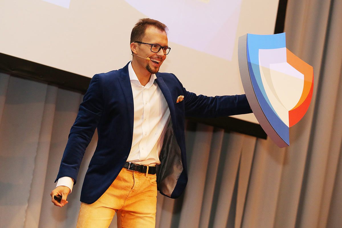 a man in a blue blazer and yellow pants holds up a shield logo