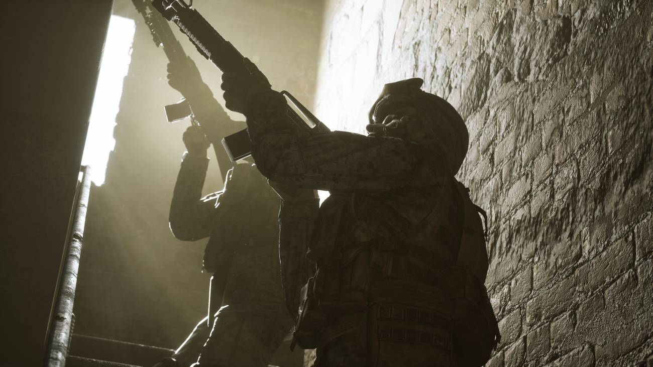 Marines move up a stairwell, backlight by a second-floor window. Light streams through the dust in the air.