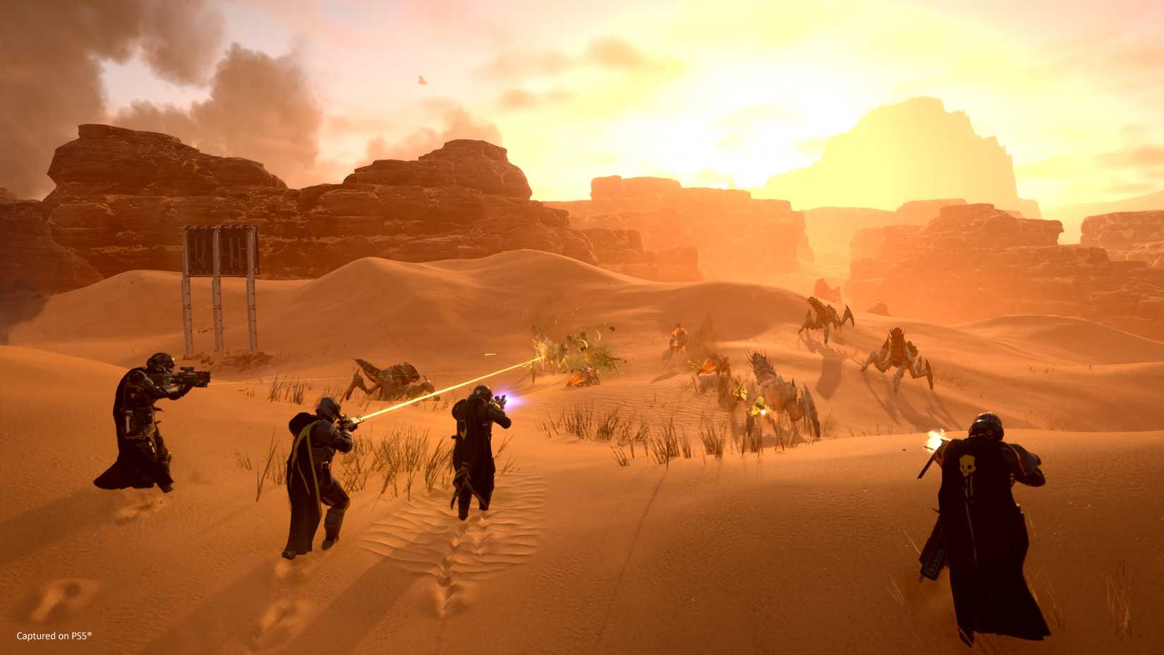 Four Helldivers fight against waves of Terminids on an arid desert planet.